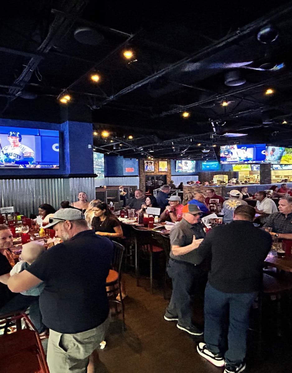 E-Tank Classic post-golf networking event at a local sports bar with teams and clients gathered for food, drinks, and conversation under multiple TV screens.